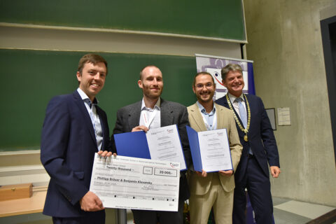 The winners of the SAOT Innovation Award, Benjamin Klevansky and Phillipp Bräuer, with Dr. Max Gmelch (left) from SAOT and the President of FAU, Prof. Joachim Hornegger (right). (Image: FAU/Boris Mijat)